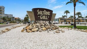 A sign for SaltRock Grill with a rocky base and palm trees in the background.
