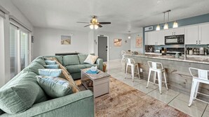 A modern living room with a sectional sofa, a coffee table, and a dining area with bar stools.