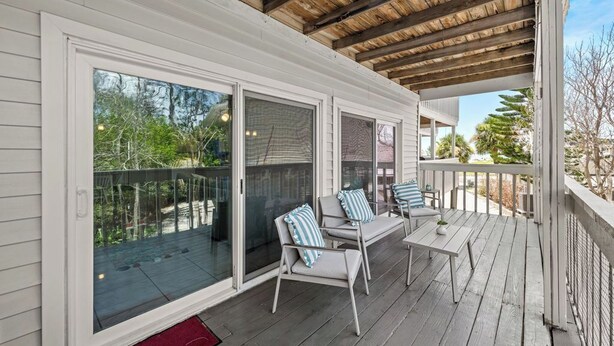 A covered outdoor area with a wooden ceiling, sliding glass doors, and a seating area with chairs and a table.