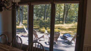 Eine Terrasse mit Holzkunststühlen und einem Tisch, mit Blick auf eine Rasenfläche mit Bäumen und einem Holzzaun.