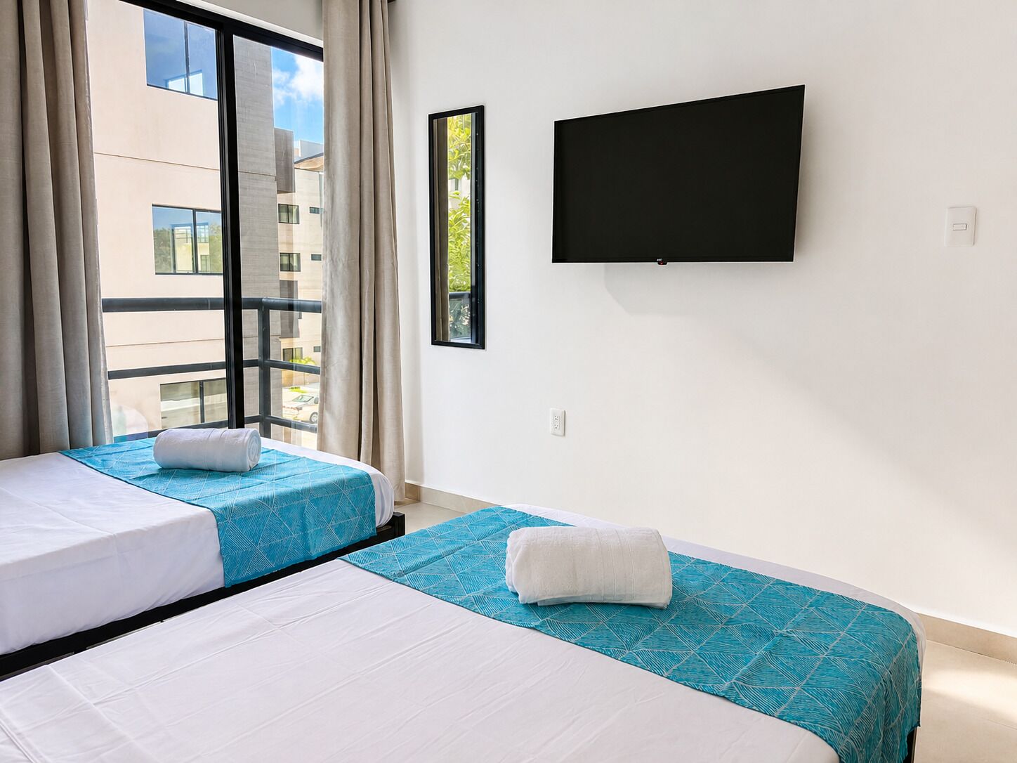 Une chambre d’hôtel avec deux lits, une grande fenêtre, un téléviseur à écran plat et une vue sur les bâtiments environnants.