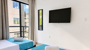Een hotelkamer met twee bedden, een groot raam, een flatscreen televisie en uitzicht op gebouwen.