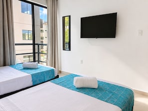 Ein Hotelzimmer mit zwei Betten, einem großen Fenster, einem Flachbildfernseher und Blick auf Gebäude.