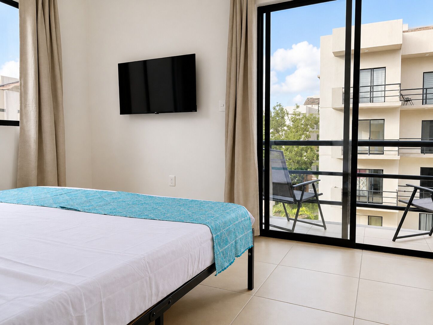 A bedroom with a bed, a TV mounted on the wall, and a balcony with a chair.