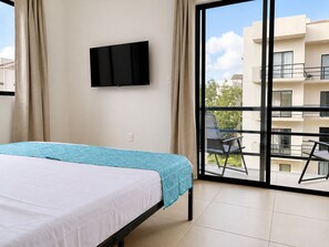 Un dormitorio con cama, televisión montada en la pared y balcón con una silla.
