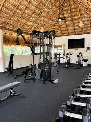 Un gimnasio con diversos equipos de ejercicio, una banca y mancuernas.