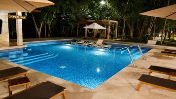 Ein Außenpool mit Liegestühlen und Sonnenschirmen, umgeben von Bäumen.