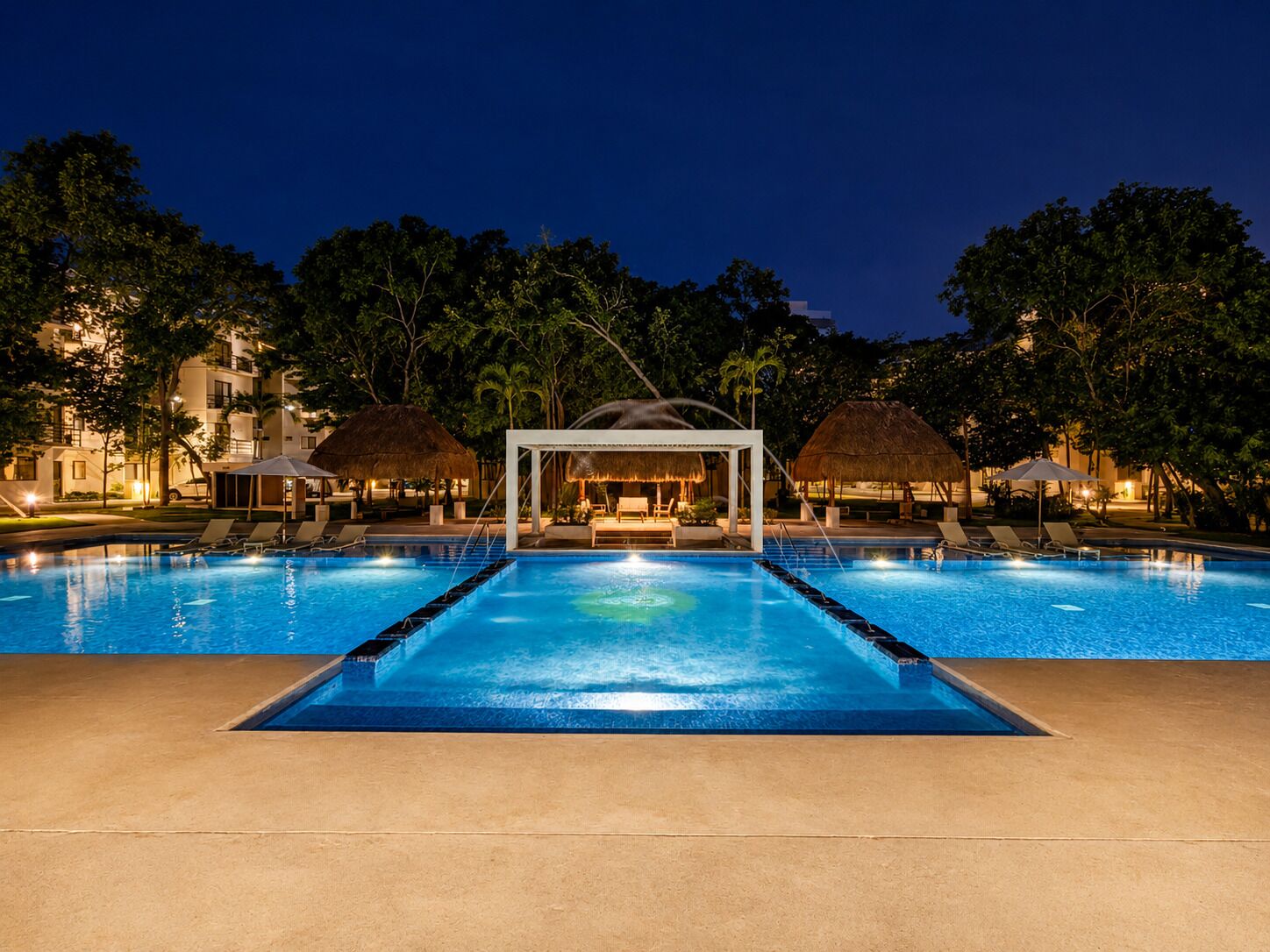 Ein Swimmingpool mit einer strohgedeckten Struktur in der Mitte, umgeben von Liegestühlen und Palmen.