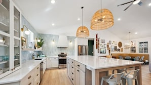Una cocina moderna con armarios blancos, una isla central, iluminación colgante y un comedor con banco.