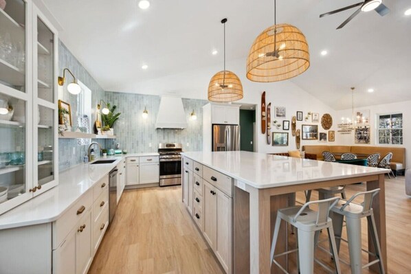 A modern kitchen with white cabinetry, a central island, pendant lighting, and a dining area with a bench.