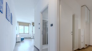 Een moderne hotelgang met een houten vloer, witte muren en een groot raam aan het einde.