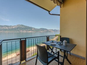 Een balkon met een tafel en stoelen met uitzicht op een wateroppervlak en verre bergen.