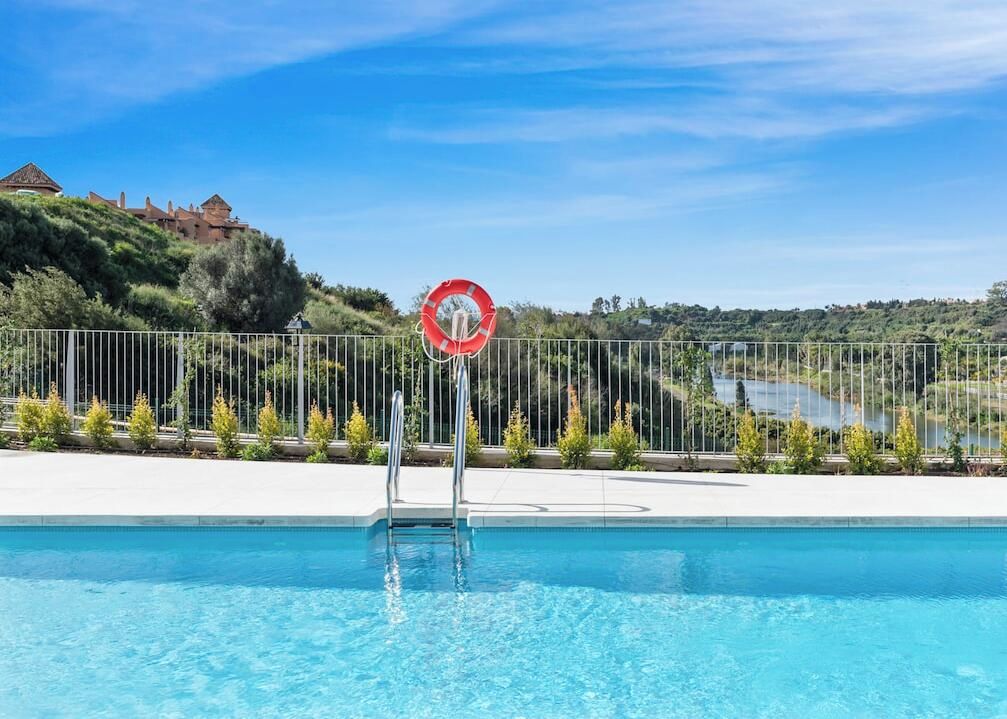 A swimming pool with a no diving sign, surrounded by a fence, with a view of a hill and a building in the background.
