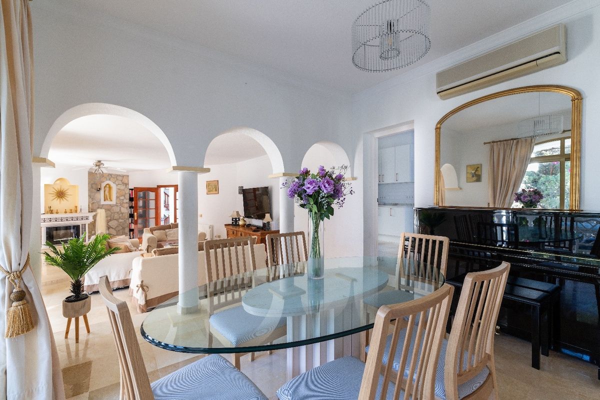 Un espace repas avec une table en verre entourée de chaises, un piano et un vase rempli de fleurs.