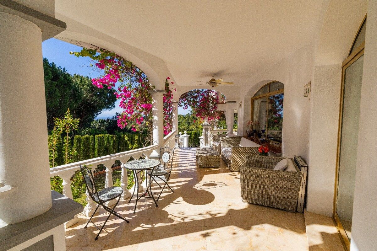 A covered outdoor seating area with wicker furniture and a view of a garden.