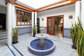 A courtyard with a fountain, potted plants, and a tiled floor.