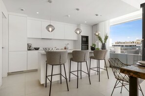 A modern kitchen with white cabinets, a central island, bar stools, and pendant lighting.