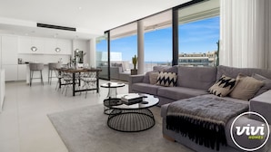 A modern living room with a grey sofa, a round coffee table, and a dining area with a wooden table and chairs.