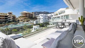 A modern hotel balcony with a pool, white buildings, and a mountain view.