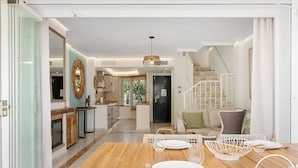 A spacious living area with a wooden dining table set for four, a kitchen in the background, and a staircase leading to an upper floor. - Lochloosa | Pool - terrace - golf (Marbella)