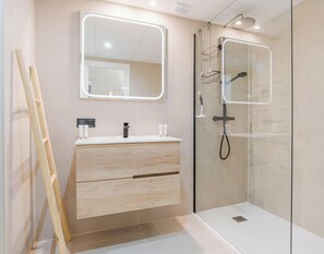 Une salle de bain moderne avec un meuble-lavabo en bois, une cabine de douche en verre et un grand miroir doté d’un éclairage intégré.