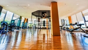 A gym with exercise equipment, large windows, and a wooden floor.