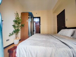 Ein Schlafzimmer mit einem Bett, einer Topfpflanze, einem Holzschrank und einer Tür zum Badezimmer.