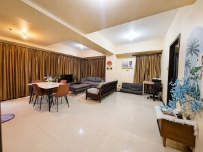 Ein modernes Wohnzimmer mit Essbereich, einer Couch, einem Fernseher und einem kleinen Tisch mit Dekoration.