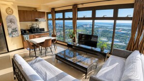 A modern living room with a dining area, a kitchen, and a large window with a city view.
