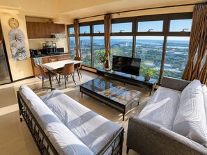 Una sala de estar moderna con comedor, cocina y un amplio ventanal con vista a la ciudad.