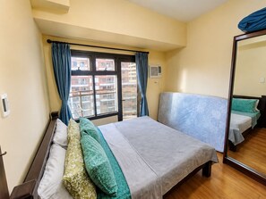 Un dormitorio con cama, mesita de noche, espejo y ventana con cortinas.