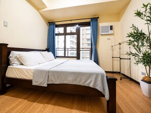 Ein Hotelzimmer mit einem Bett, einem Fenster mit Vorhängen, einer Topfpflanze und einer Klimaanlage.