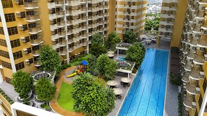 Un edificio residencial de gran altura con varios balcones, una piscina central y una zona de juegos infantiles.