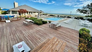 A wooden deck with a pool, lounge chairs, and a view of the ocean. - Your Lake Erie Islands' Getaway Condo for 6 with a Clubhouse and Pool! (Port Clinton)