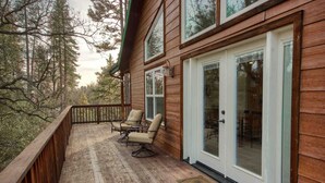 A wooden deck with two chairs, a glass door, and a view of trees. - Red Tail Retreat in Mariposa (Mariposa)
