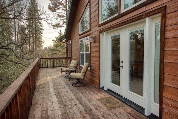 A wooden deck with two chairs, a glass door, and a view of trees.