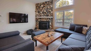 A living room with a stone fireplace, a large window, and a flat-screen TV. - Red Tail Retreat in Mariposa (Mariposa)