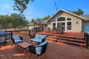 A deck with outdoor furniture, a barbecue grill, and a house with large windows and a covered porch.