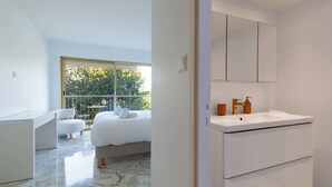 Een moderne hotelkamer met een groot bed, een glazen bureau en een balkon met uitzicht op groen.