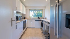 Een moderne keuken met witte kasten, een geïntegreerde vaatwasser, een roestvrijstalen koelkast en een raam voor natuurlijk licht.