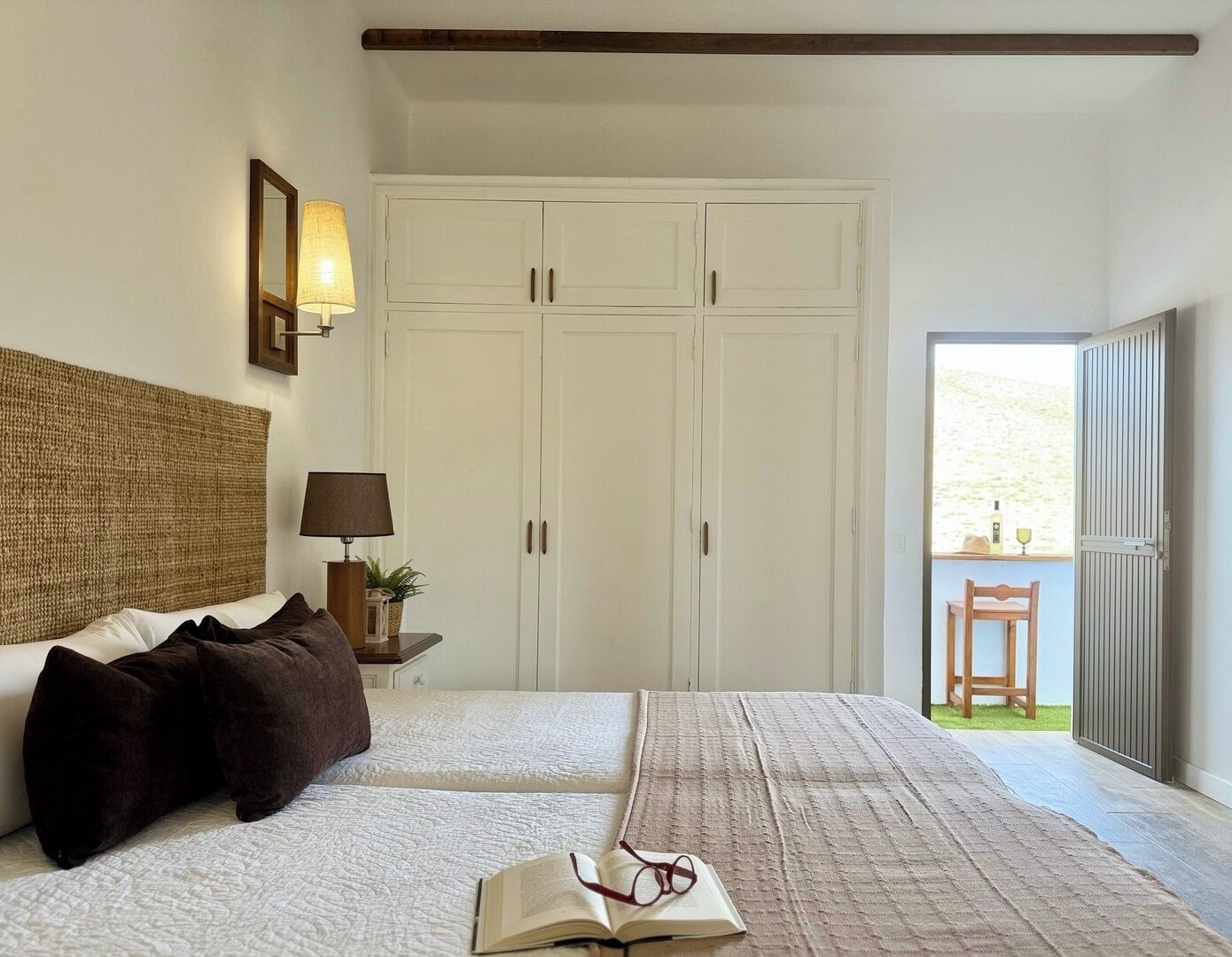 Een slaapkamer met twee bedden, een kledingkast, een nachtkastje met een lamp, en uitzicht op de omgeving.