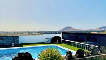 Un área de piscina moderna con una vista despejada de una montaña y una masa de agua al fondo.