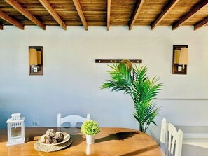Un coin repas avec une table en bois, des chaises blanches, une plante en pot et des lampes fixées au mur.