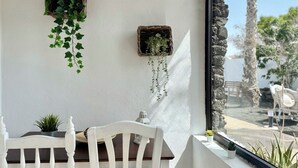 A balcony with a white chair, a small table, and two hanging planters with green plants. - Canaryislandshost l Olympica 7 (Tahiche)