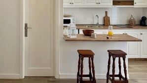 A kitchen with white cabinets, a wooden countertop, two stools, and a hanging light fixture. - Canaryislandshost l Olympica 7 (Tahiche)