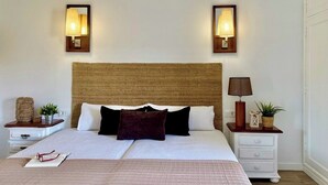 A neatly made bed with a woven headboard, two bedside tables with lamps, and a bedside plant. - Canaryislandshost l Olympica 7 (Tahiche)