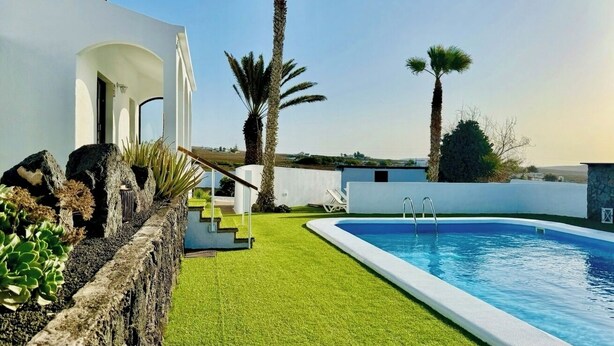 Un área de piscina moderna al aire libre con una piscina azul cristalina, un muro de piedra y un césped bien cuidado.