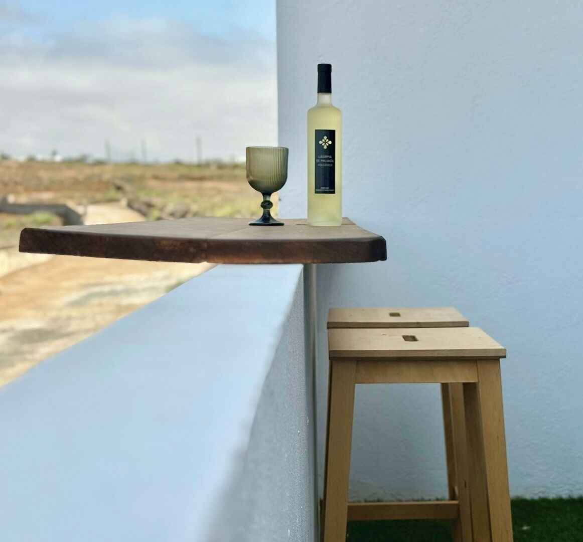 Ein kleiner Holztisch mit einer Weinflasche und einem Glas auf einer schwebenden Ablage neben einem Fenster mit Blick auf eine Landschaft.