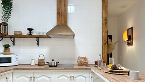 A kitchen with white cabinets, a microwave, a stove, and a wooden shelf with decorative items. - Canaryislandshost l Olympica 5 (Tahiche)