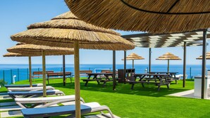 A beachside patio with thatched umbrellas, lounge chairs, and picnic tables.